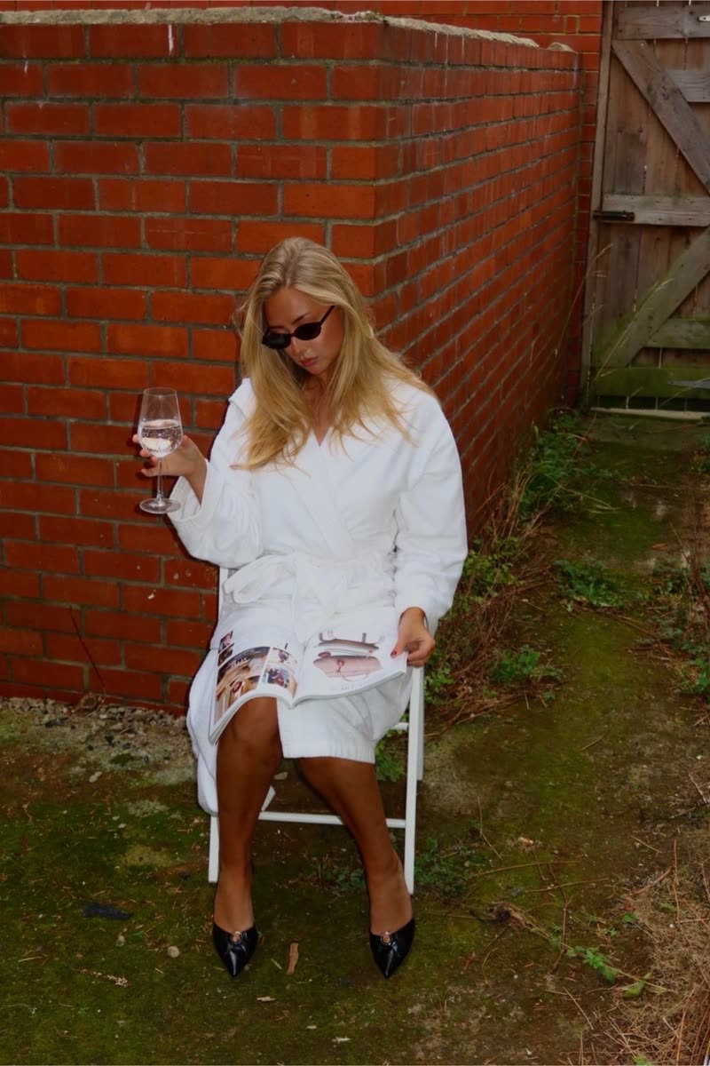 Reading a magazine with a glass of wine, in a white robe and black pointed heels