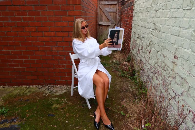 Reading a magazine on a folding chair in a brick-walled yard