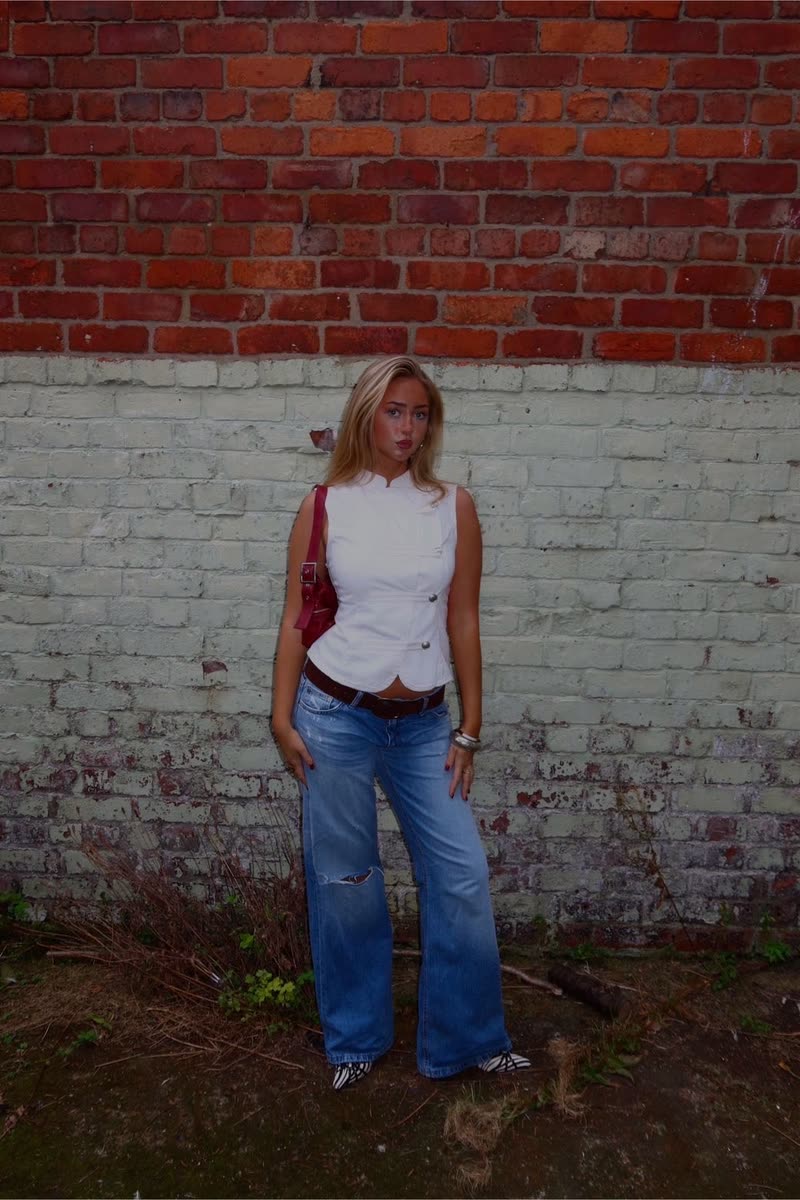 Full-length look: white waistcoat, wide-leg blue jeans and a red shoulder bag