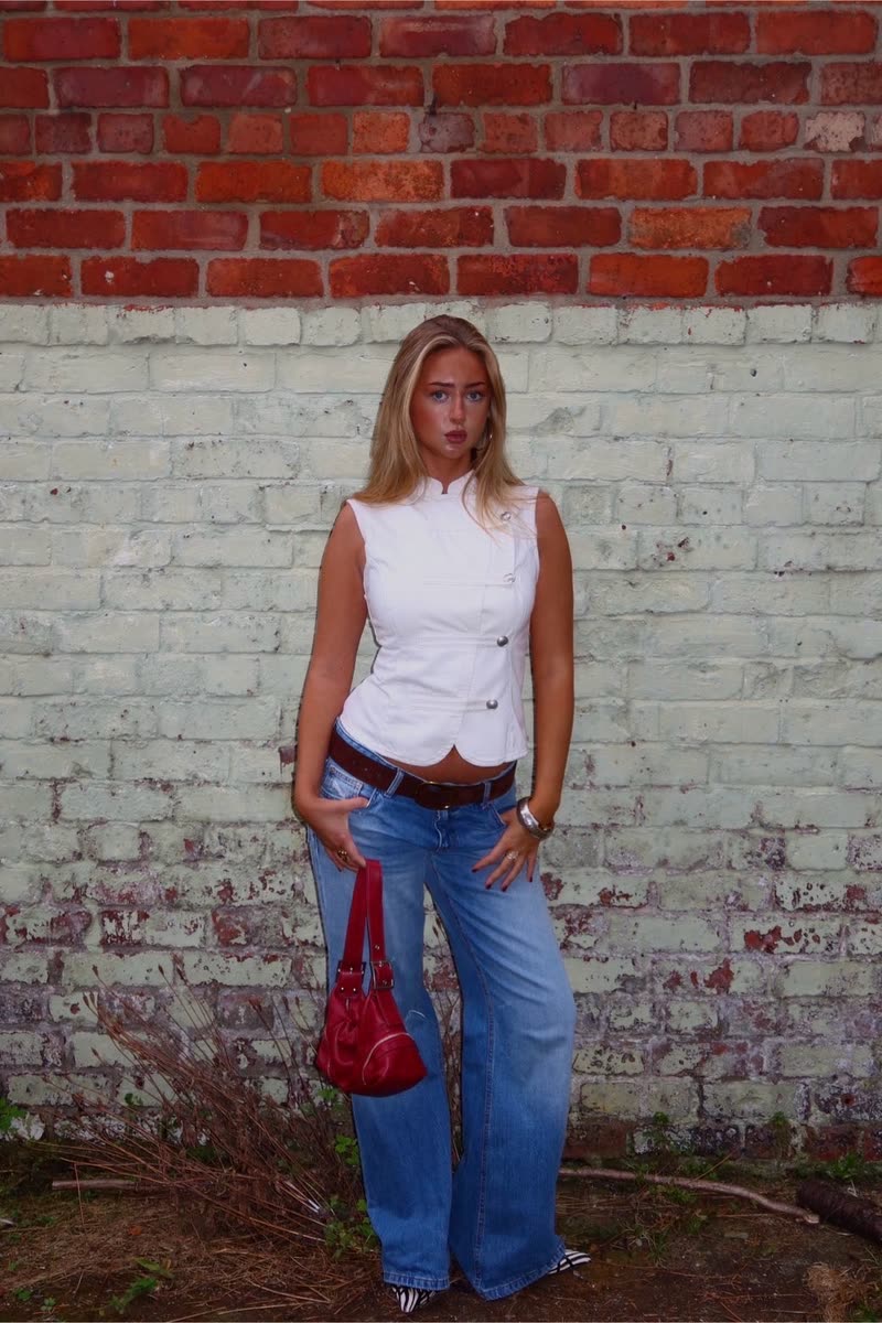 Holding a red bag, styled with a white waistcoat and low-rise wide-leg denim